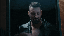 a man in a leather jacket is looking at himself in a mirror with a w logo on the bottom right