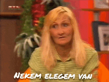 a woman with blonde hair is sitting in front of a sign that says nekem eleget van