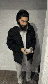 a man in a black jacket and grey sweatpants is holding a can