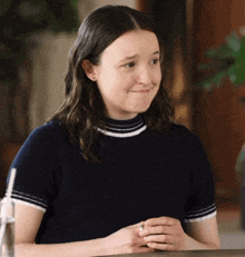 a young woman in a black and white striped shirt is sitting at a table with her hands folded