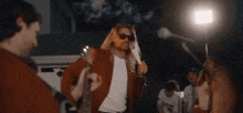 a man with long blonde hair is singing into a microphone while holding a guitar