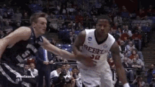 two basketball players are playing a game of basketball on a court in front of a crowd .