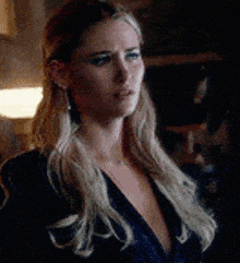 a woman with long blonde hair is wearing a blue dress and earrings and looking at the camera .
