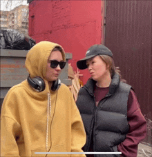 two women standing next to each other one wearing headphones and the other wearing a hat