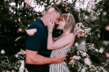 a man and woman are kissing in a garden with petals falling from the trees