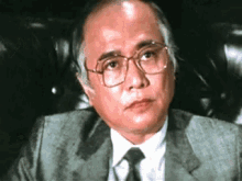 a man in a suit and tie is sitting in a chair and looking at the camera .