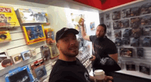 two men are standing in front of a wall of toys and a monopoly board game