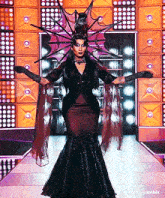 a drag queen is walking down a runway wearing a costume that looks like a witch .