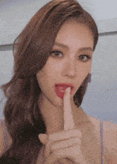a woman holds her finger to her mouth while wearing a purple top