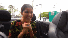a woman wearing a floral shirt is smiling in the back seat of a car