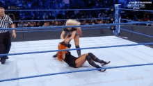 two women are wrestling in a ring with a referee watching .