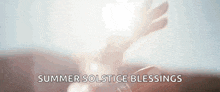 a close up of a person 's hand holding a candle with the words `` summer solstice blessings '' written above it .