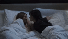 two women laying on a bed with white sheets