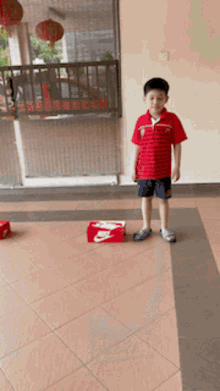 a boy in a red shirt stands next to a nike box