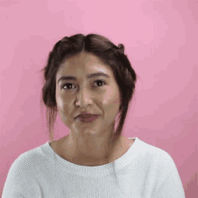a woman wearing a white sweater is smiling against a pink backdrop