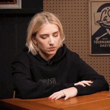 a woman sits at a table wearing a black sweatshirt that says swosh