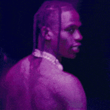 a man with dreadlocks and a necklace on his neck is standing in a dark room .