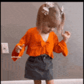 a little girl wearing an orange top and a black skirt is dancing in a room .