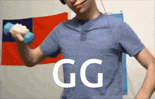 a man in a blue shirt is lifting a blue dumbbell in front of a flag that says gg on it