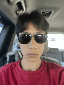 a young man wearing sunglasses and a red shirt looks at the camera