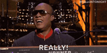 a man wearing sunglasses is singing into a microphone while playing a keyboard and saying `` really '' .