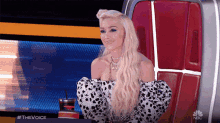 a woman with blonde hair is sitting in a chair with a cup of coffee and a nbc logo on the bottom