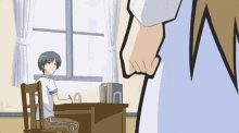 a boy sits at a desk in front of a window while a girl stands in front of him