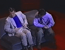 two men are sitting on a couch and talking