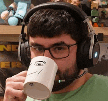 a man wearing headphones and glasses is drinking from a coffee mug .