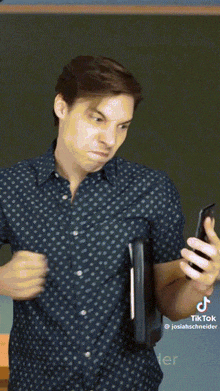 a man in a polka dot shirt is holding a book and looking at his cell phone