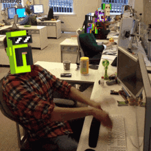 a man sitting at a desk with a green block on his head that says t