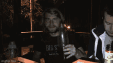 a man wearing a big sta shirt holds a glass of beer