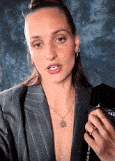 a woman wearing a necklace with a compass on it is talking