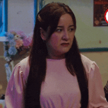 a woman in a pink shirt is standing in a room and looking at the camera .