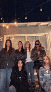 a group of young women are posing for a picture with their arms crossed in front of a window .