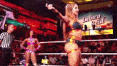 two women are standing in a wrestling ring while a referee stands behind them .