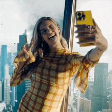 a woman in a plaid shirt is taking a selfie with a yellow phone