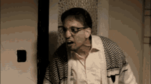 a man wearing glasses and a plaid sweater is standing in front of a door