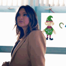a woman in a tan jacket stands in front of a window with a picture of an elf on it