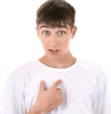 a young man wearing a white shirt is pointing at his chest .