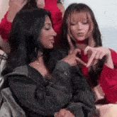 a group of young women are sitting next to each other and making a heart shape with their hands .