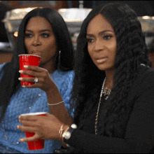 two women sitting next to each other drinking red cups
