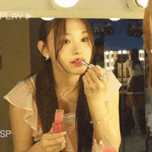 a woman is applying lipstick in front of a mirror with the word play on the bottom