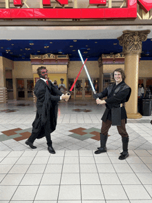 two men dressed as darth maul and anakin skywalker holding lightsabers in front of a sign that says ' x '