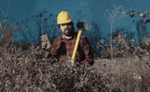 a man wearing a hard hat and plaid shirt is holding a yellow shovel