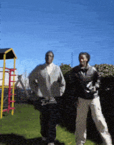 two men are dancing in front of a playground with one wearing a sweater that says ' ea ' on it