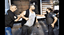 a man is being held by two police officers one of whom is wearing a black vest with the word police on it