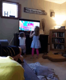 two little girls standing in front of a tv with a sign on the wall that says " be thou my vision "