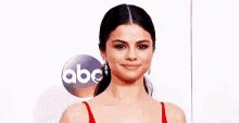 selena gomez is wearing a red dress and earrings and smiling .