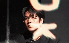 a young man wearing glasses and a necklace is looking at the camera .